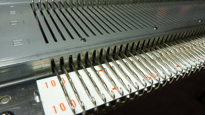 Not Enough Needles Full-length view of a knitting machine's needlebed showing the fixed number of needles available, illustrating the width limitations machine knitters face when creating larger pieces