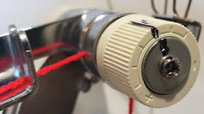 Thread it right Close-up photo of a knitting machine's tension assembly, showing detailed view of the numbered tension dial and threading area