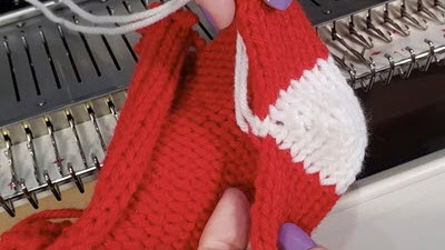 6 Tips for Knitting Socks A sock being knitted on a flatbed knitting machine, showing the work in progress with visible short row shaping for the heel area