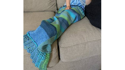 Mermaid Tail: Why should crocheters have all the fun? A toddler snuggled inside a knitted mermaid tail blanket with textured stitch patterns, showing the practical use of this cozy children's accessory