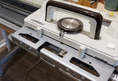 Buying a used Machine? Ask Questions A knitting machine carriage positioned on the needle bed, ready for operation - a key component to inspect when buying a used machine