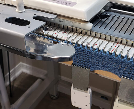 Photograph of a knitting machine showcasing the carriage placed on the left, illustrating its setup for specific knitting techniques. Knitting machine with carriage positioned on the left side