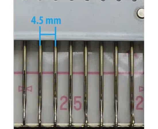 Visual example of needle pitch on a knitting machine with labeled spacing Close-up of knitting machine needle spacing